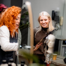 Two women interacting in a casual setting with a third person partially visible.