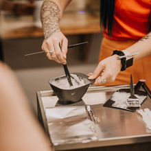 Person mixing hair color in a bowl with a brush on a counter.