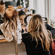 Two women working together on a project with mannequins and materials in a workshop setting.